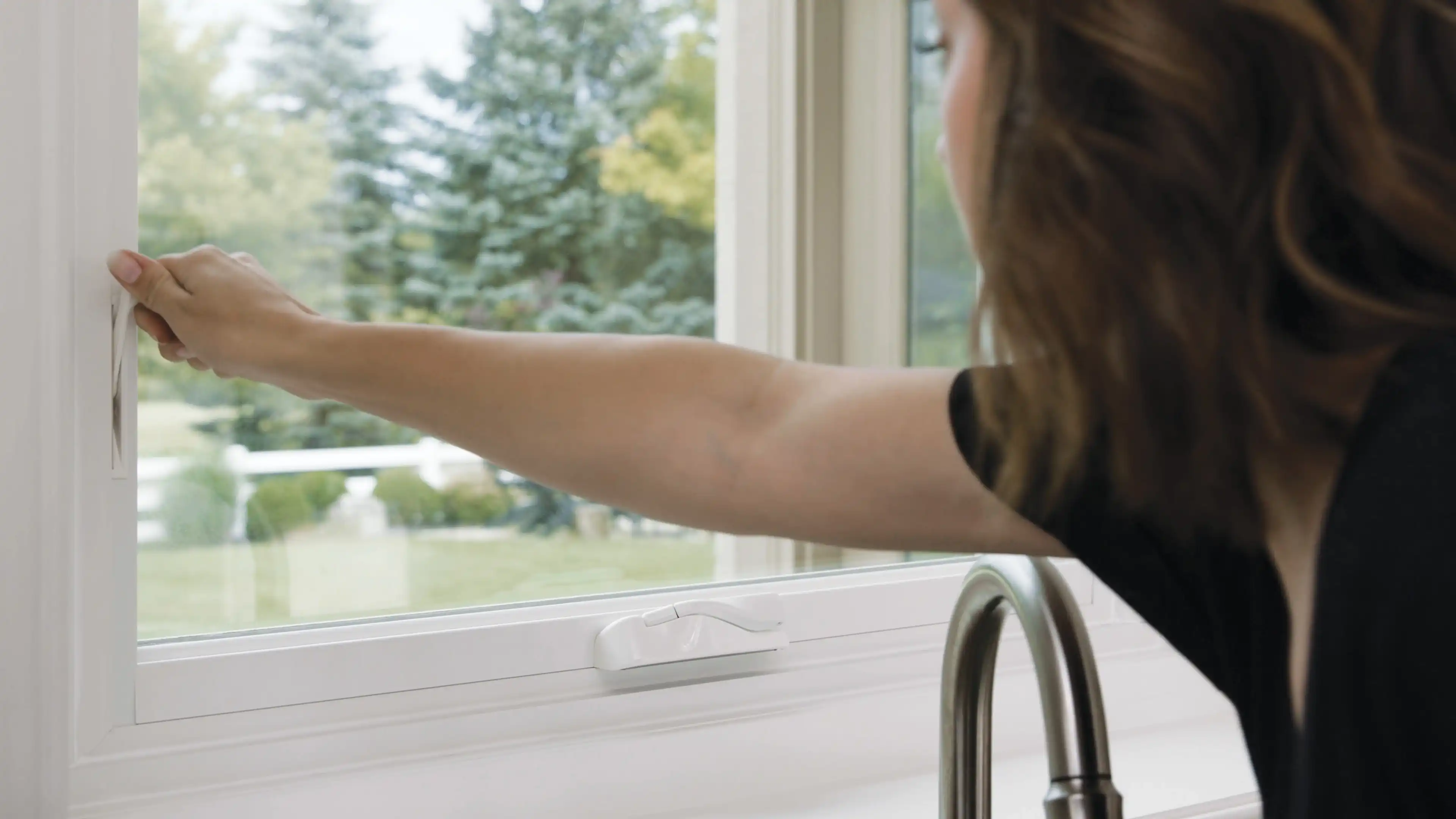 Woman reaches for a white Marvin Replacement Casement window latch to lock the window.