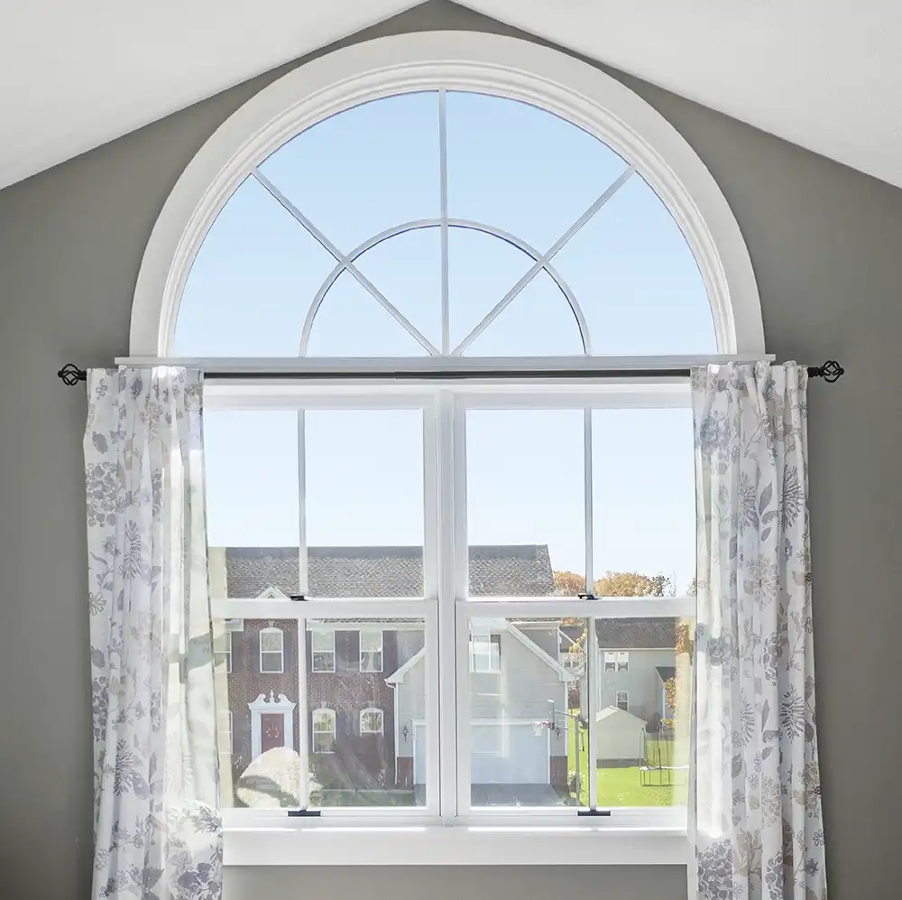 Interior view of a white arch window with grilles above two double hung windows.