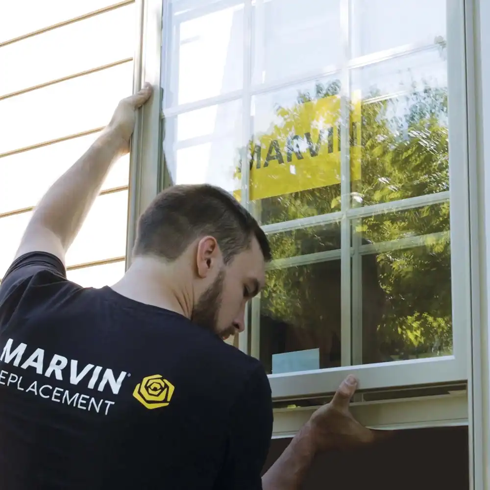 Man with a beard installs a window from the exterior of a home.